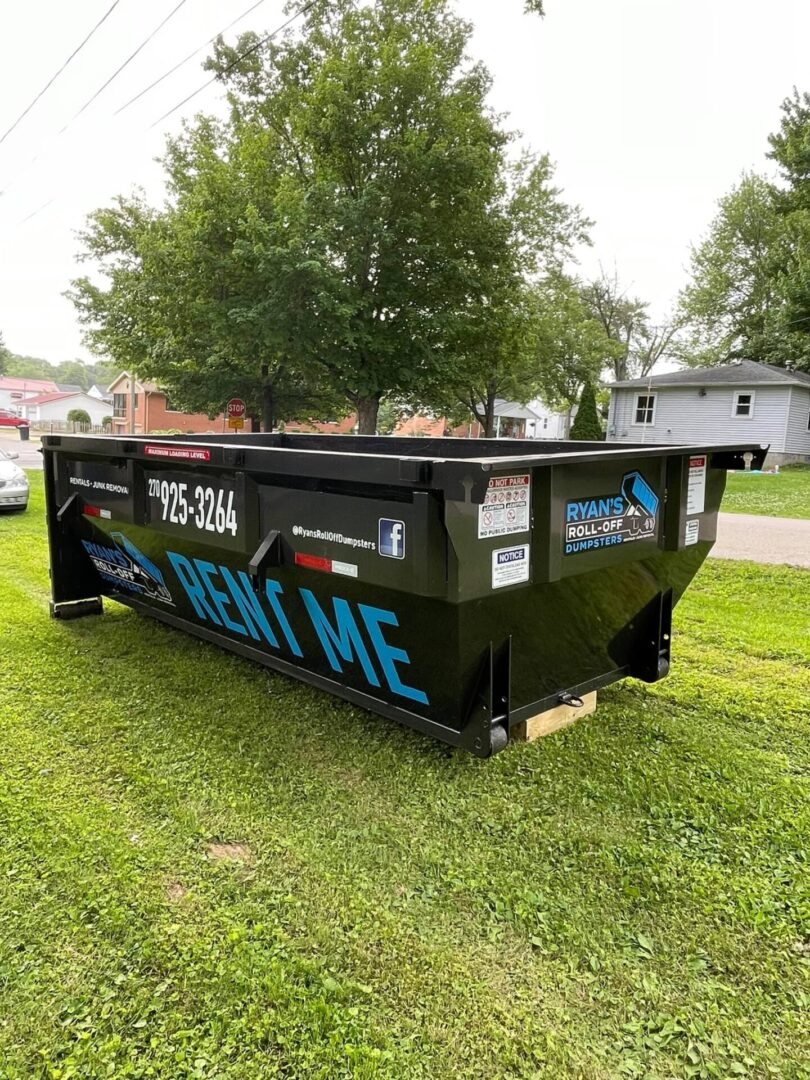 A dumpster sitting in the grass next to some trees.